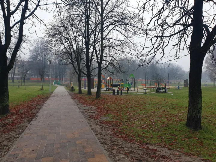 W tle plac zabaw i siłownia plenerowa