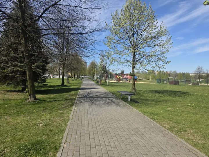 Brukowana aleja parkowa, po prawej stronie plac zabaw dla dzieci