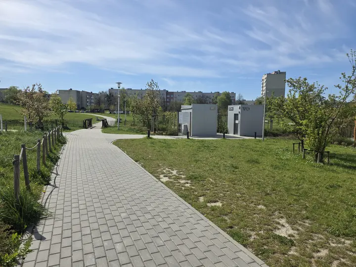 Parkowa alejka z toaletami publicznymi po prawej stronie