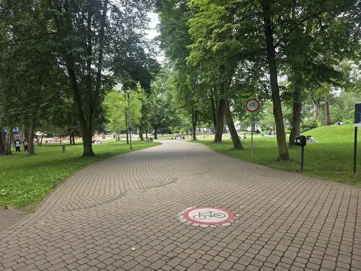 Znak zakazu wjazdu rower&oacute;w, a w oddali po lewej stronie widoczny jest plac zabaw dla dzieci