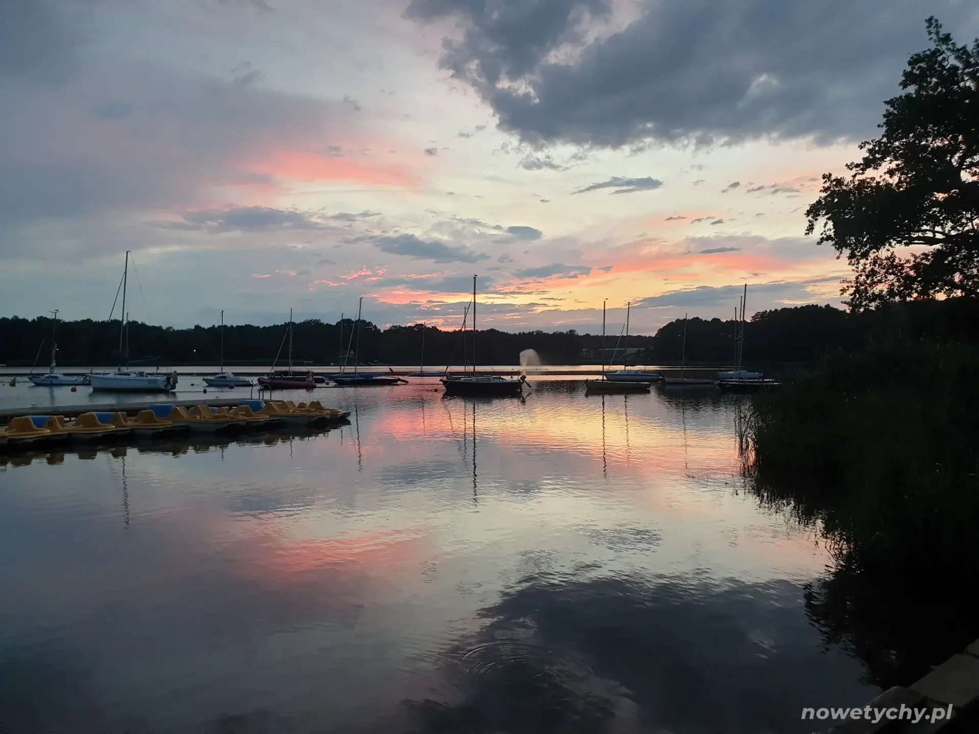 Widok na zacumowane żagl&oacute;wki i rowerki wodne - po zachodzie słońca