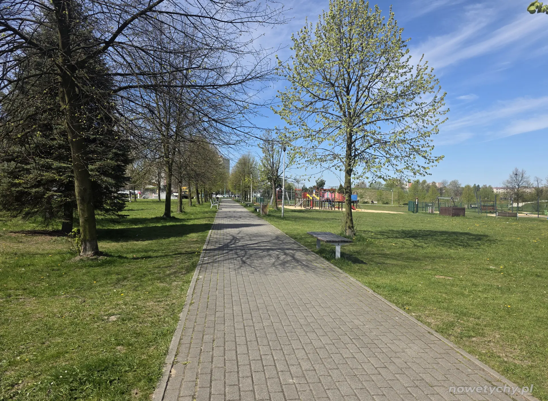Brukowana aleja parkowa, po prawej stronie plac zabaw dla dzieci