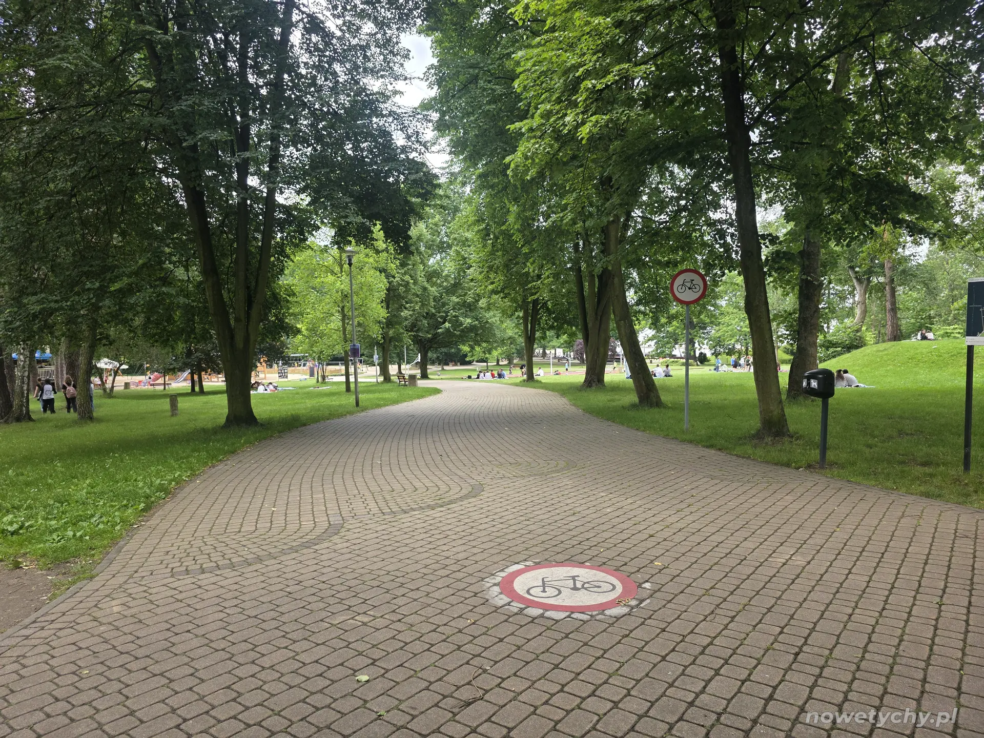 Znak zakazu wjazdu rower&oacute;w, a w oddali po lewej stronie widoczny jest plac zabaw dla dzieci